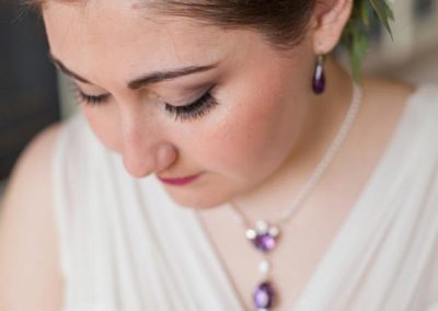 A woman wearing a white dress and purple necklace.