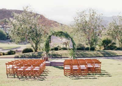 A wedding ceremony with wooden chairs and an arch.