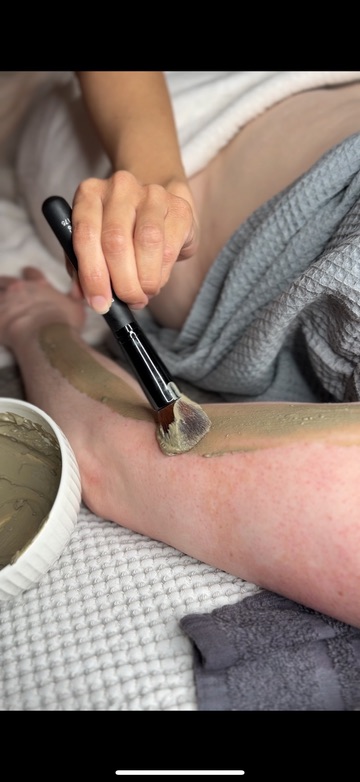 Botanical clay brushed onto the leg during a detoxifying body wrap